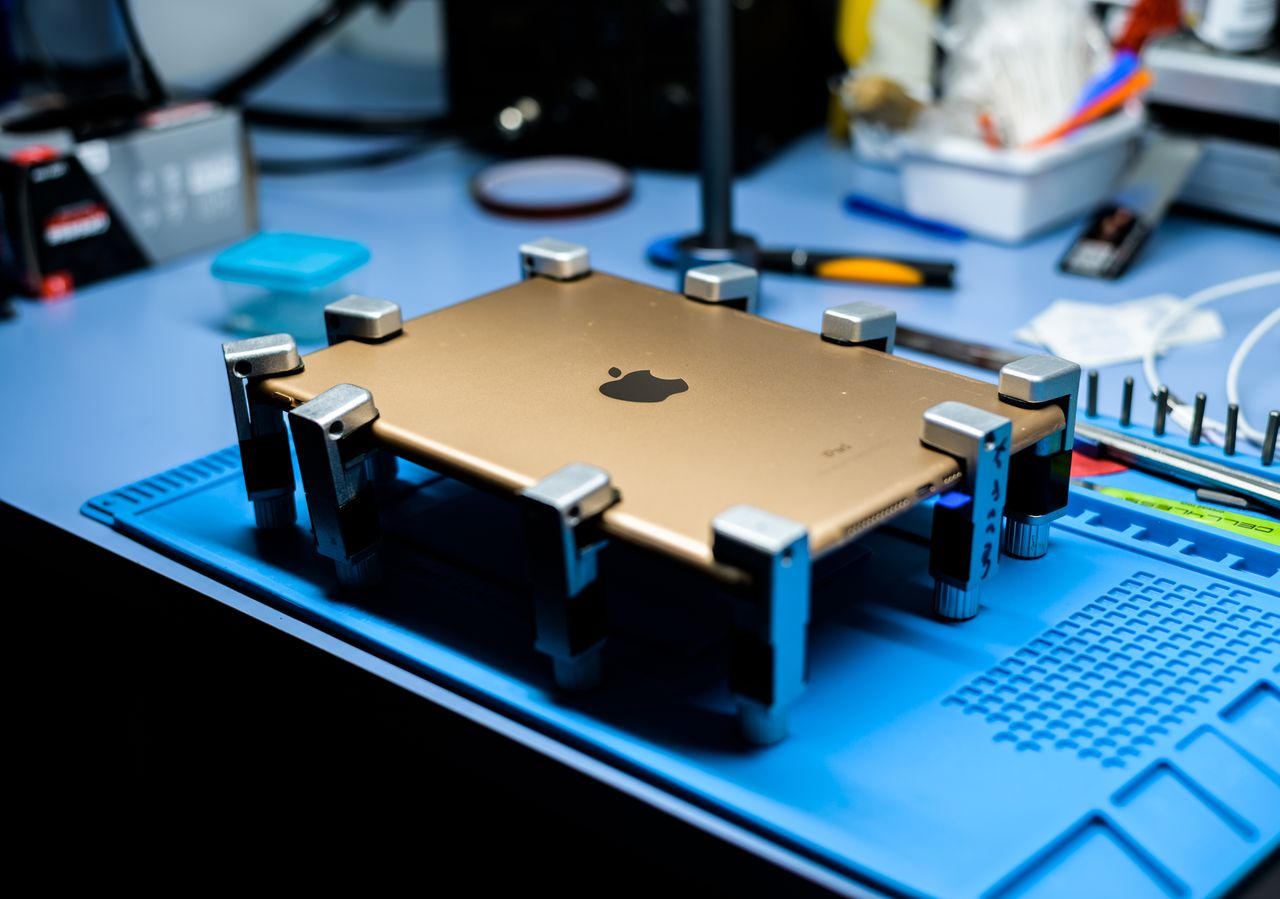 portfolio-03 A close-up view of a tablet undergoing repair in a tech workshop with specialized tools.