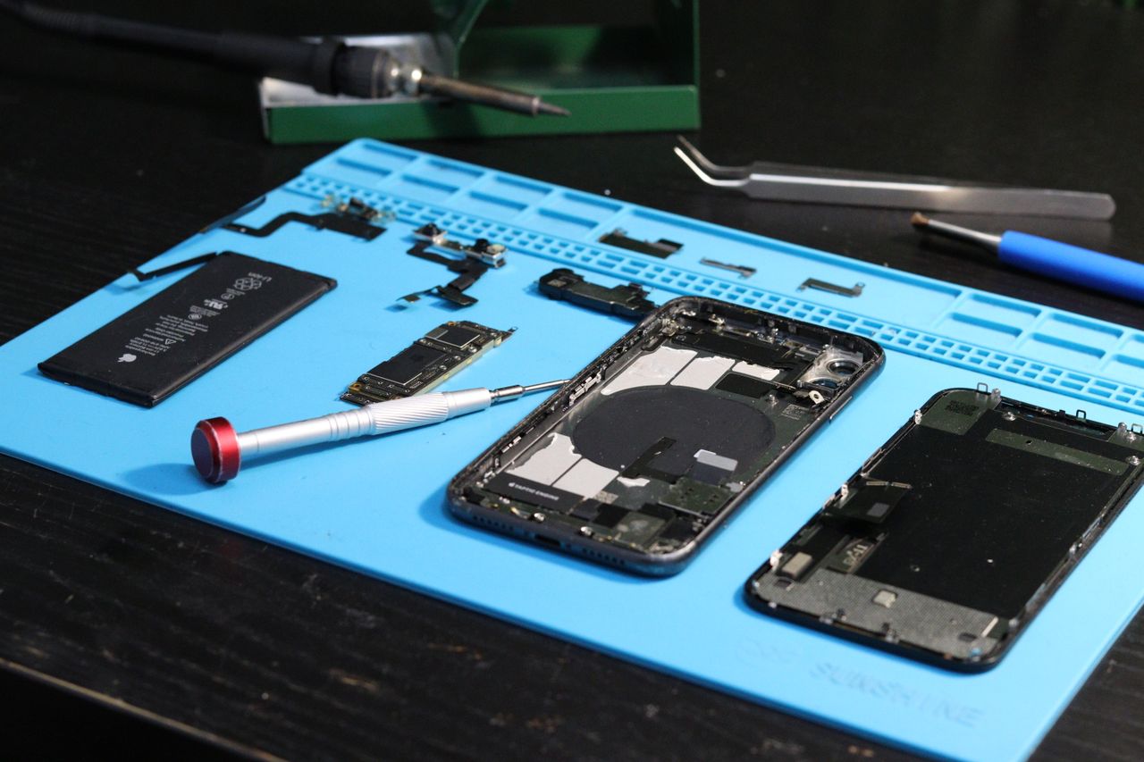portfolio-06 Close-up of disassembled smartphone parts on a blue repair mat with tools.