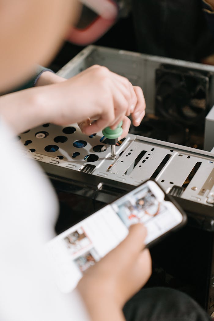 why-choose-us Hands using screwdriver to repair computer hardware, referencing smartphone for guidance.