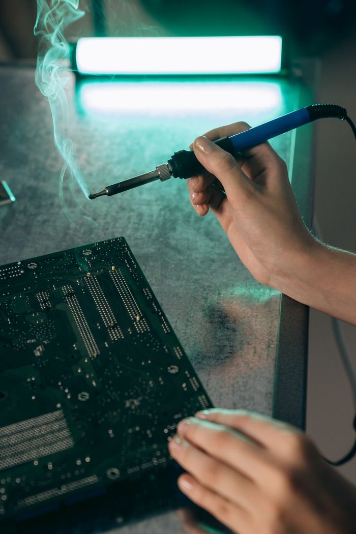 portfolio-04 Close-up of hands working on a motherboard with a soldering iron, producing smoke.